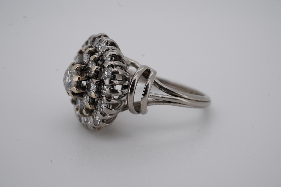 A white metal and diamond cluster set dress ring, with 'wire work' shoulders, size H, gross weight 5.2 grams. Condition - fair to good